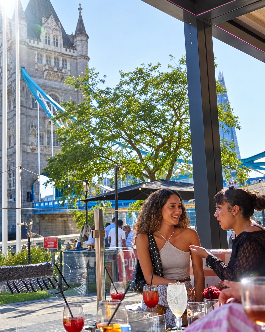 Guests enjoying cocktails on a sunlit river terrace beneath Tower Bridge